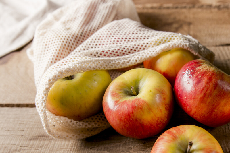 A group of red and yellow apples spilling out of a mesh bag onto a wooden surface.