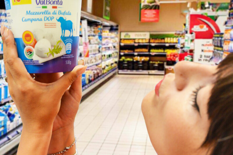 A person is holding a container of ValBontà Mozzarella di Bufala Campana DOP in a grocery store aisle.